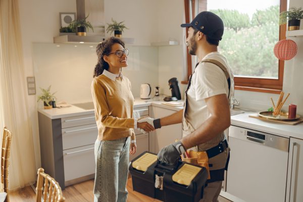 Professional male handyman shaking hands with happy female client while standing at home kitchen
